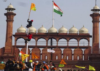 A Sikh man hangs on to pole holding a Sikh flag along with a farm union flag at the historic Red Fort monument in New Delhi, India, Tuesday, Jan. 26, 2021. Tens of thousands of protesting farmers drove long lines of tractors into India's capital on Tuesday, breaking through police barricades, defying tear gas and storming the historic Red Fort as the nation celebrated Republic Day. (AP Photo/Dinesh Joshi)