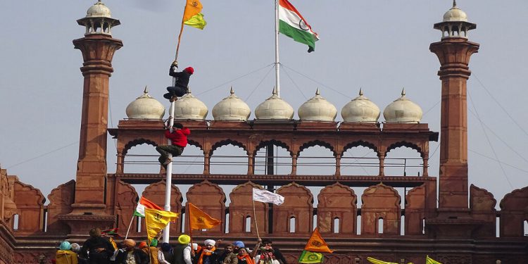 A Sikh man hangs on to pole holding a Sikh flag along with a farm union flag at the historic Red Fort monument in New Delhi, India, Tuesday, Jan. 26, 2021. Tens of thousands of protesting farmers drove long lines of tractors into India's capital on Tuesday, breaking through police barricades, defying tear gas and storming the historic Red Fort as the nation celebrated Republic Day. (AP Photo/Dinesh Joshi)