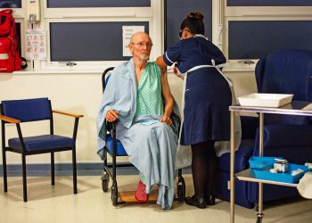 FILE - In this Tuesday Dec. 8, 2020 file photo, "Bill" William Shakespeare, 81, receives the Pfizer-BioNTech COVID-19 vaccine, at University Hospital, Coventry, England. On Friday, Dec. 11, 2020, The Associated Press reported on stories circulating online incorrectly asserting the first two recipients of the COVID-19 vaccine in Britain are “crisis actors.” At University Hospital Coventry on Dec. 8, nurse May Parsons first administered the vaccine to Margaret Keenan, 90, then to “Bill” William Shakespeare.(Jacob King/Pool via AP)