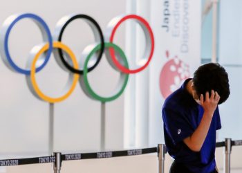 A staff standing in front of Olympic rings reacts while waiting for the arrival of foreign athletes at Haneda Airport ahead of Tokyo 2020 Olympic Games, in Tokyo, Japan July 8, 2021. REUTERS/Kim Kyung-Hoon