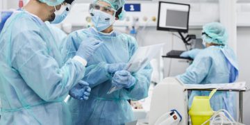 Male and female doctors discussing while standing in ICU. Healthcare workers are protective workwear. They are at hospital.