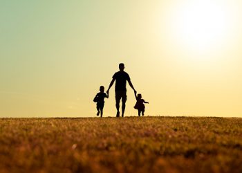 Father walking with his kids in the park at sunset.