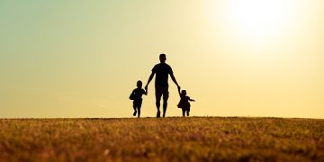 Father walking with his kids in the park at sunset.