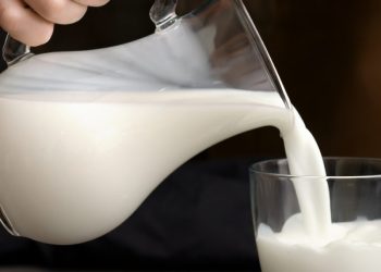 Woman pouring fresh milk from jug into glass on table